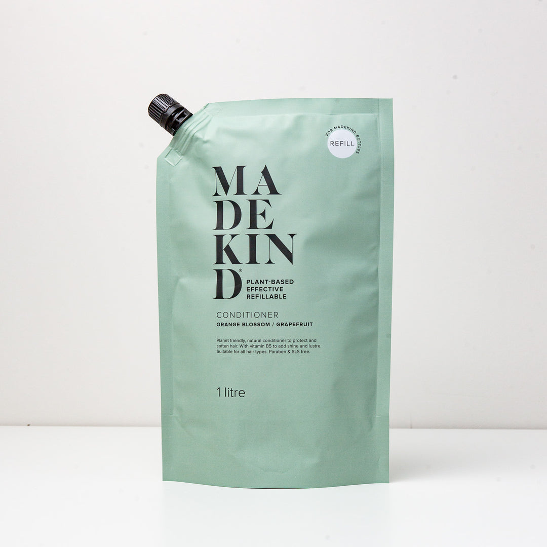 A green pouch labeled 'MADEKIND' containing hair conditioner. The packaging indicates it is a 1 litre refill of conditioner with orange blossom and grapefruit scents.