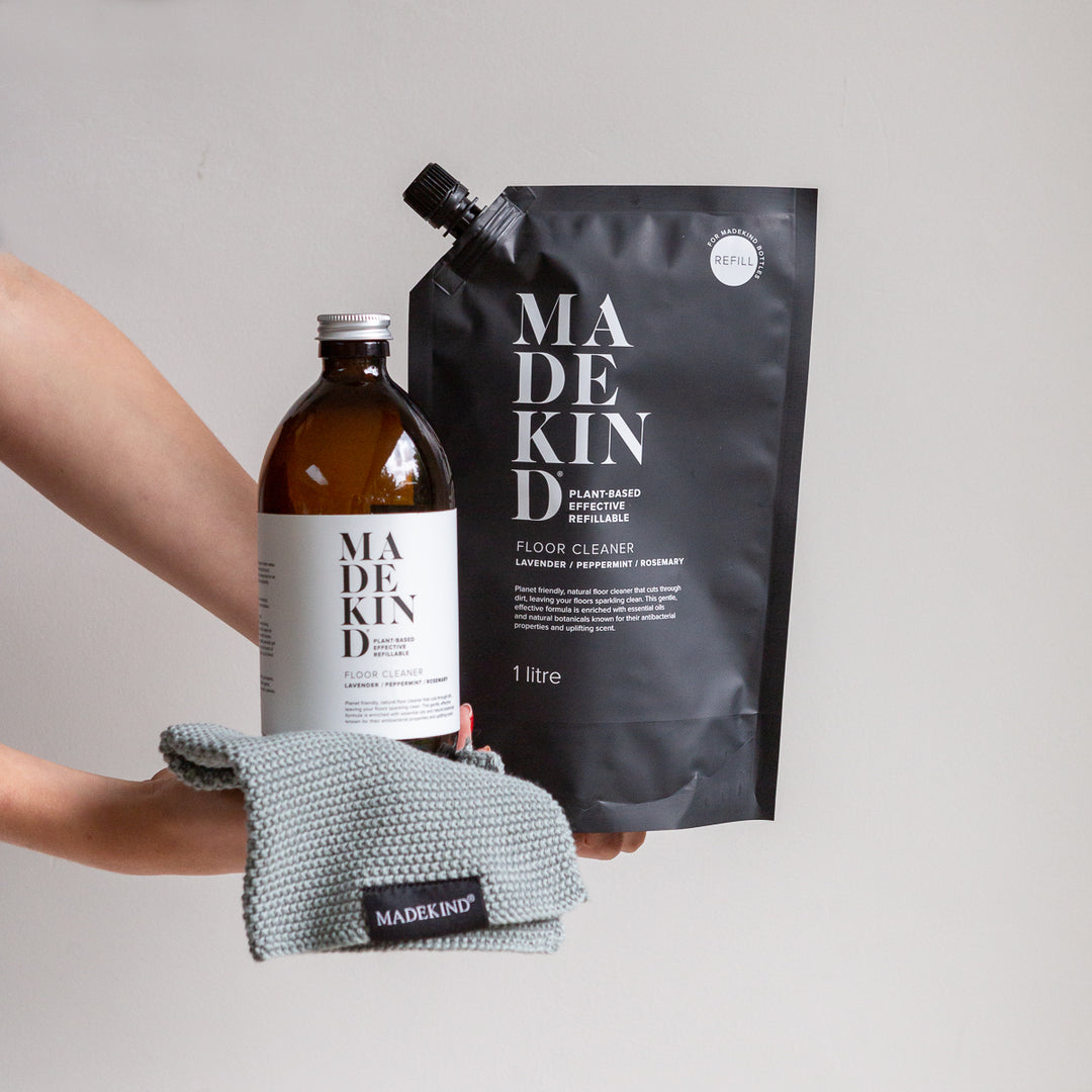 Photo of hands holding MadeKind Floor Cleaner refill pouch and an empty amber glass bottle and an organic cotton dish cloth
