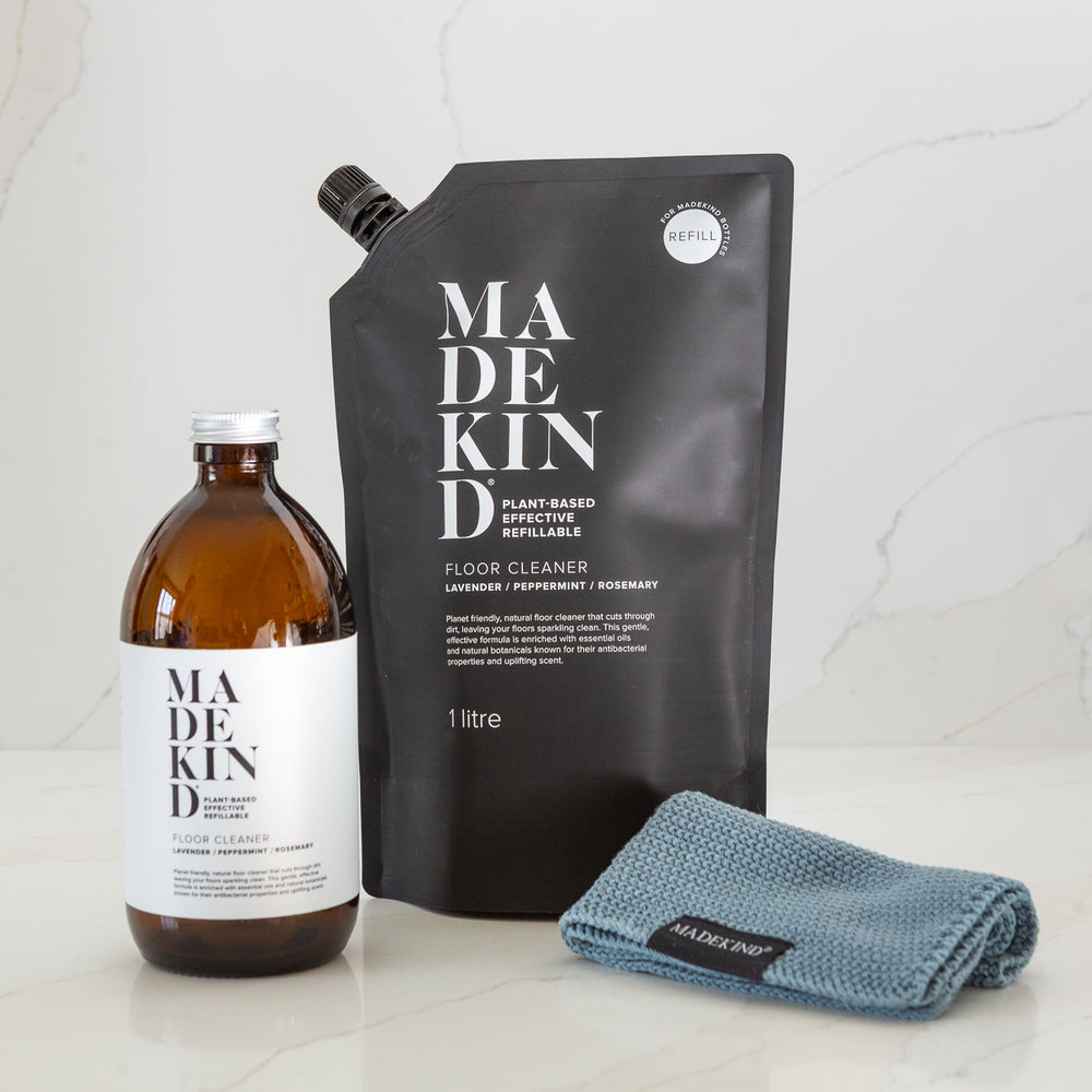 MadeKind floor cleaner glass bottle, refill pouch, and blue cloth on a light background. eco friendly cleaning products.