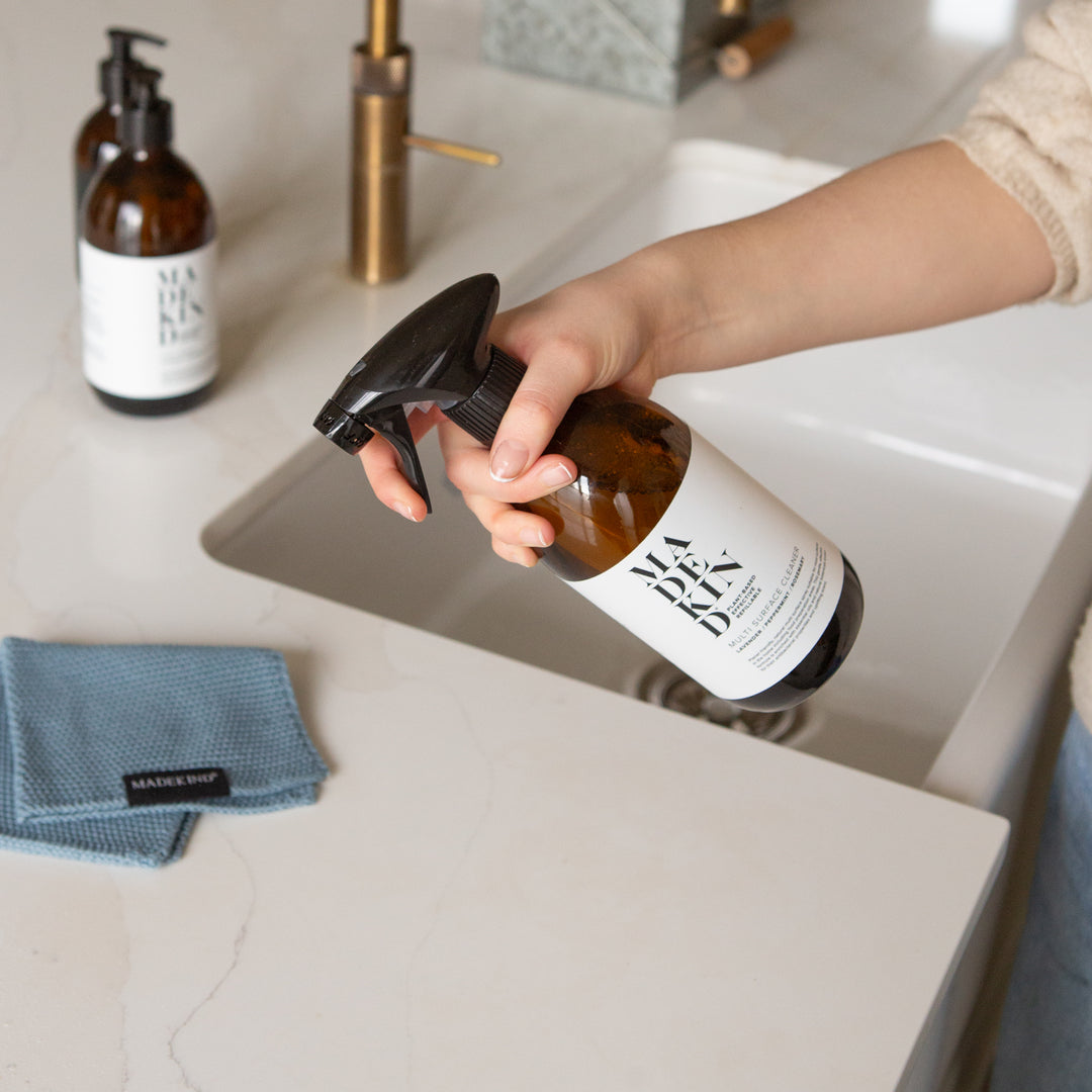 Photo of a hand holding a bottle of Multi Surface Cleaner at a kitchen sink