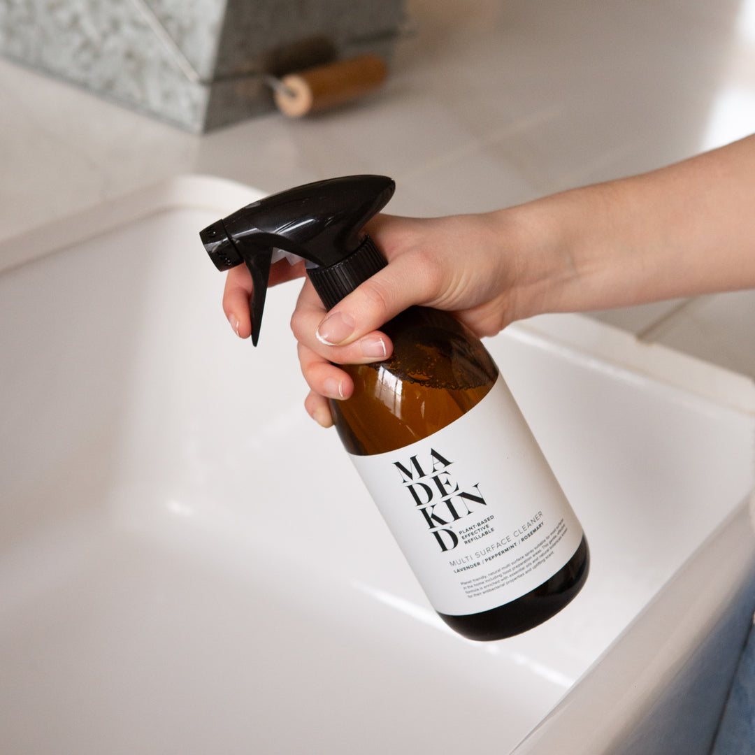 Photo of a hand holding MadeKind Natural Multi Surface Cleaner in an amber glass bottle