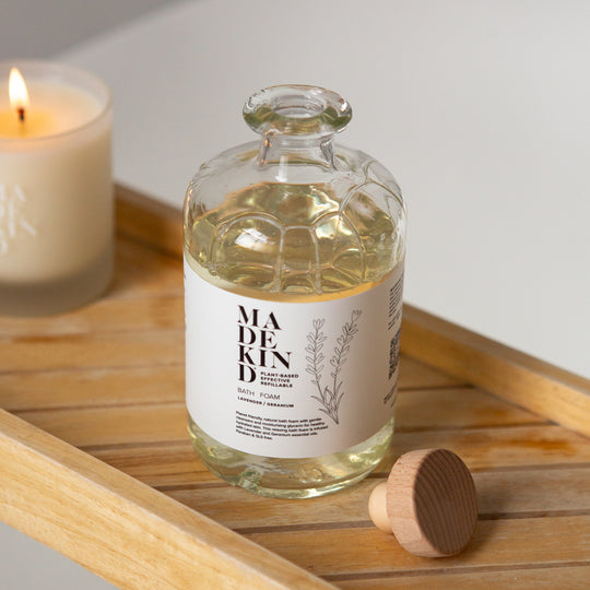 Bottle of MadeKind Bath Foam on a wooden tray with a candle in the background