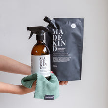 Load image into Gallery viewer, Photo of stretched out arms holding out an amber glass bathroom cleaner bottle and a 1 litre refill pouch and an organic cotton dish cloth
