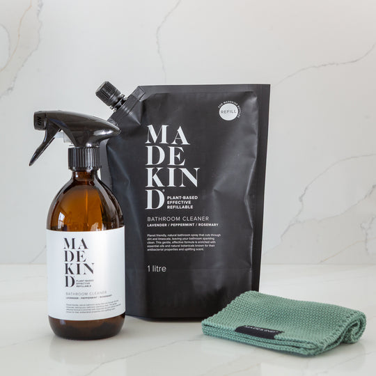Madekind cleaning products including a spray bottle, 1 litre refill pouch and green cloth on a light background