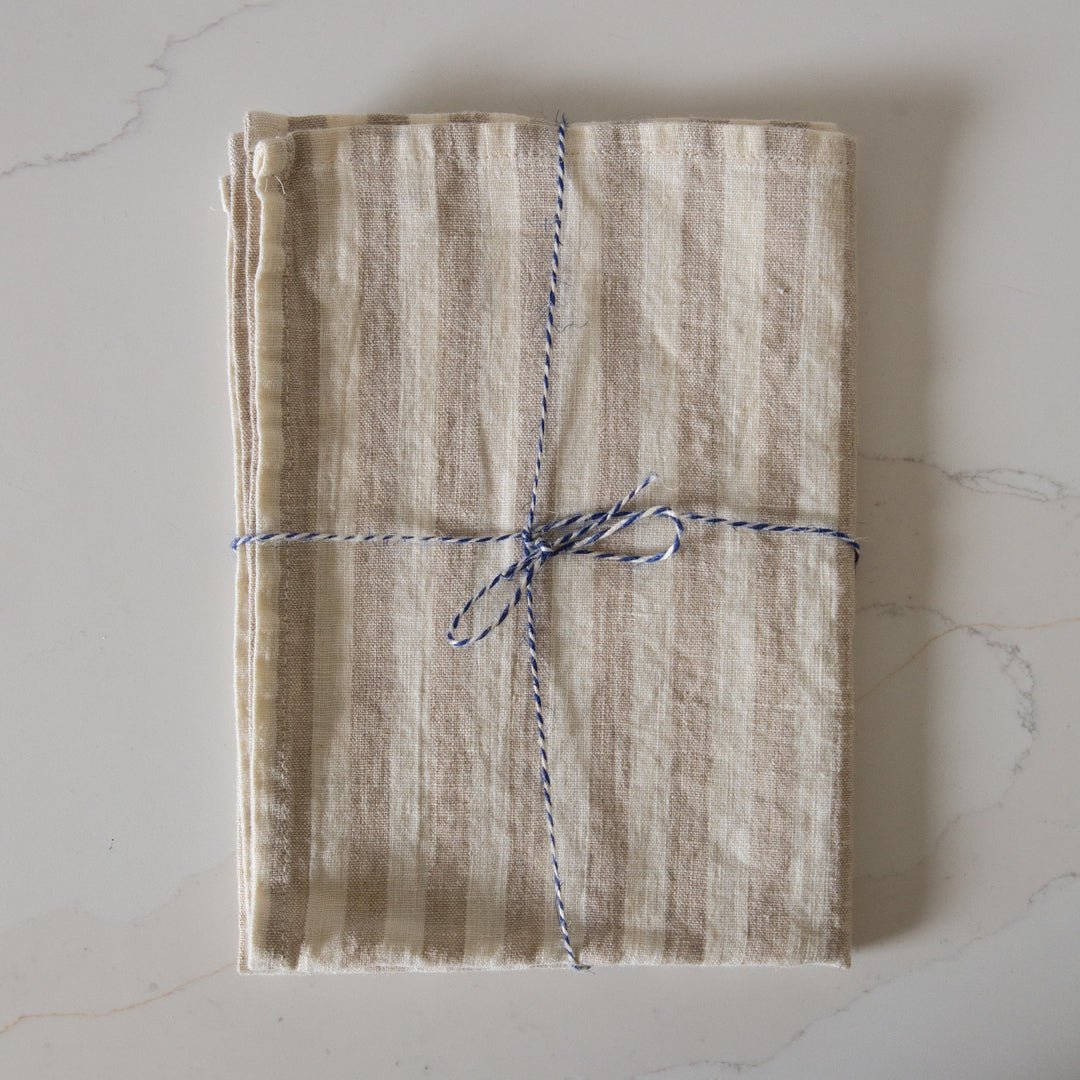 Photo of a woven line beige and white striped tea towel, folded and tied with twine