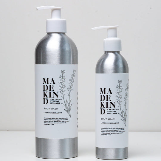 Two silver pump bottles of MADE KIND body wash with white labels, one larger and one smaller, standing on a white surface against a light gray background.