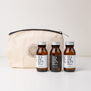 Photo of cotton pouch with MadeKind logo and 3 mini toiletries. 60ml amber glass bottles of shampoo, body wash and hand wash.