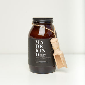 Photo of an amber glass jar of MadeKind bath salts with a wooden scoop