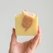 Load image into Gallery viewer, Photo of MadeKind natural soap bar with lemongrass &amp; ginger essential oils, held in a hand

