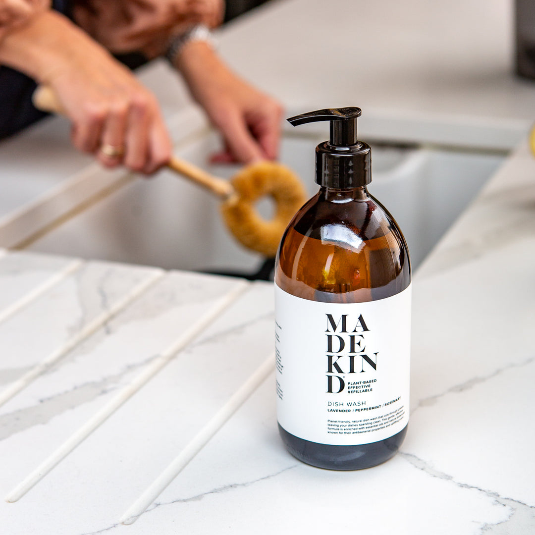 Amber glass bottle with pump labeled 'MADE IN' on a marble countertop with a person cleaning in the background.
