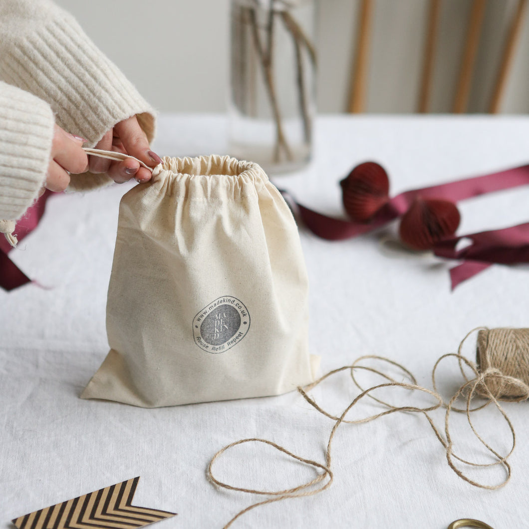 photo of a cotton MadeKind gift bag with MadeKind logo stamped on front, being held in hands