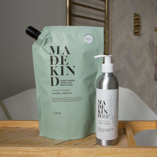 MadeKind conditioner refill pouch and a metal pump bottle of conditioner on a wooden tray in a bathroom setting.