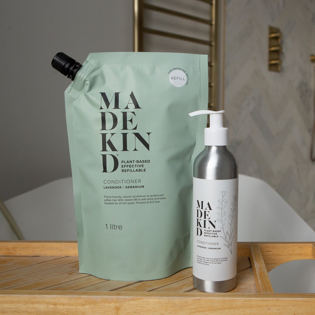 MadeKind conditioner refill pouch and an aluminium pump bottle of conditioner on a wooden tray in a bathroom setting.