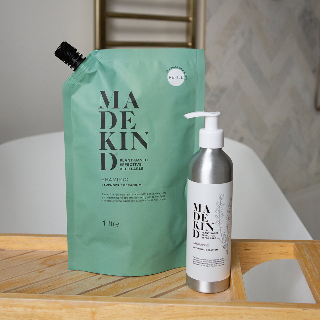 MadeKind Shampoo Refill next to a refillable aluminium shampoo bottle on a bath tray across a bath