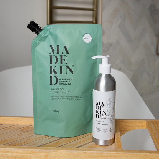 MadeKind Shampoo Refill next to a refillable aluminium shampoo bottle on a bath tray across a bath