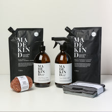 Load image into Gallery viewer, Photo of the MadeKind Kitchen Cleaning Kit; Multi Surface Cleaner and Dish Wash refills with 2 empty amber glass bottles, copper scourers and grey dishcloths
