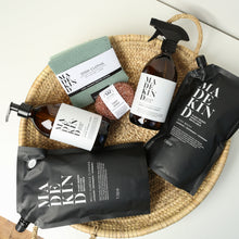 Load image into Gallery viewer, Photo of the MadeKind Kitchen Cleaning Kit in a basket; Multi Surface Cleaner and Dish Wash refills with 2 empty amber glass bottles, copper scourers and green dishcloths
