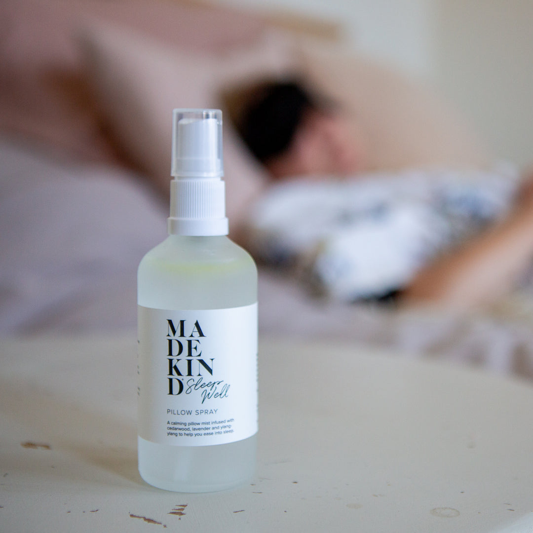 Photo of a sleep spray in a bedside table with somone asleep in background