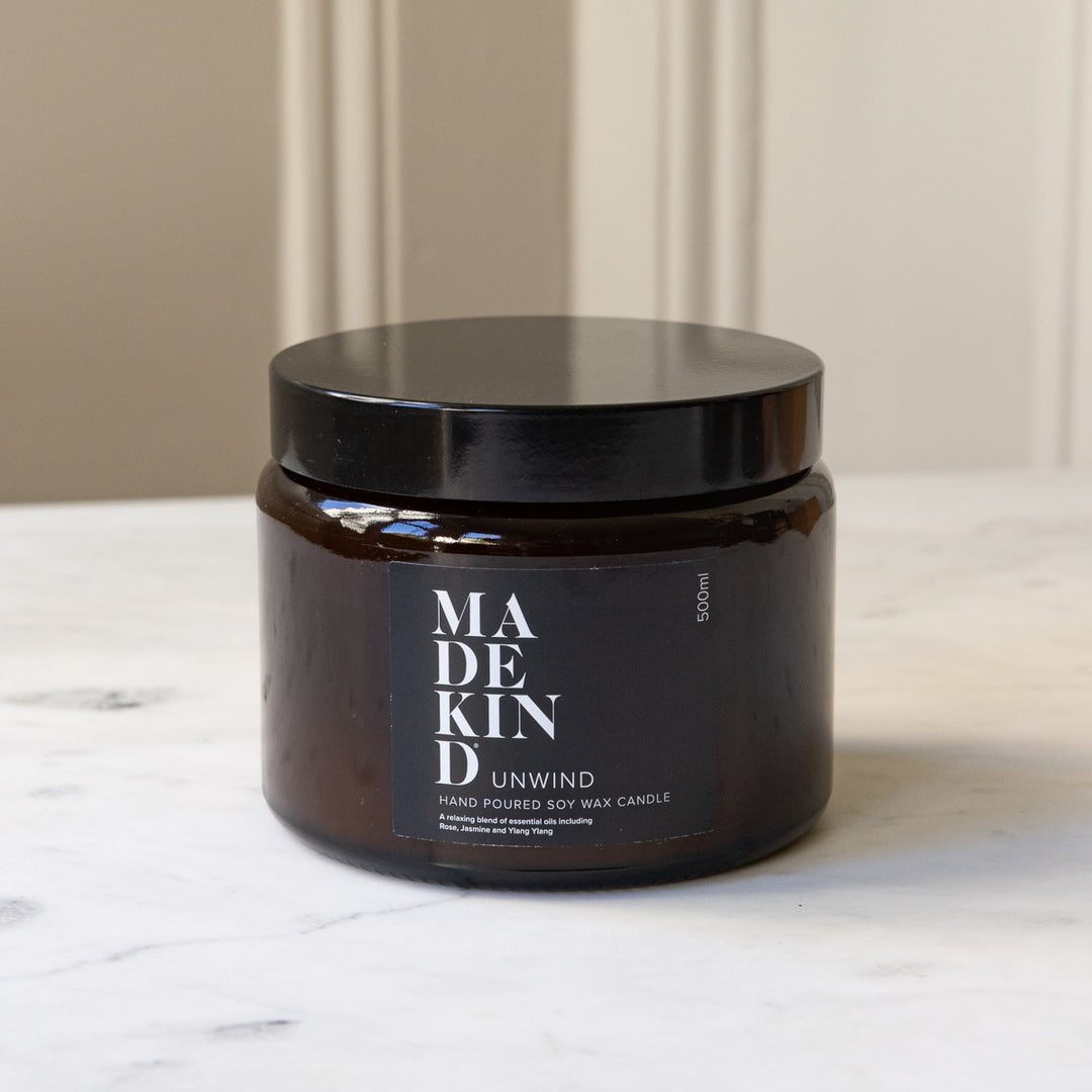 An amber glass jar MadeKind soy wax candle with three wicks on a light marble surface. The jar is amber and lid is black.
