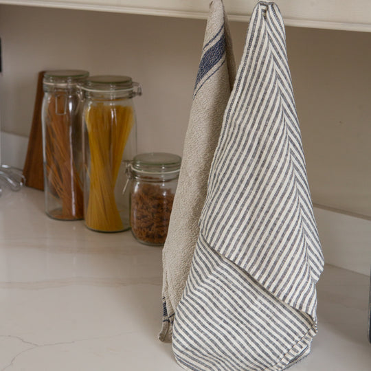 Photo of a woven linen grey striped tea towel and a rustic tea towel hung in a kitchen