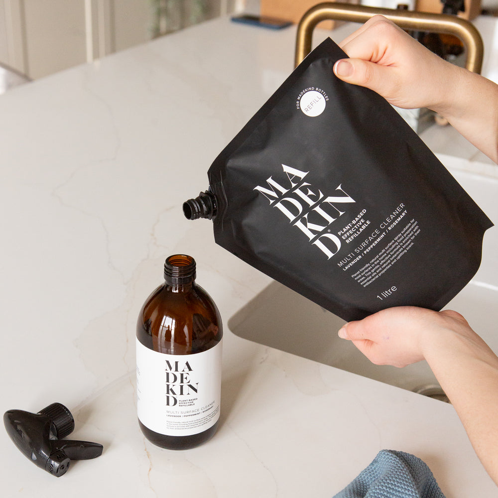 Photo of a MadeKind 1 Litre Multi Surface Cleaner Refill pouch being poured into an empty MadeKind forever amber glass bottle on a kitchen counter