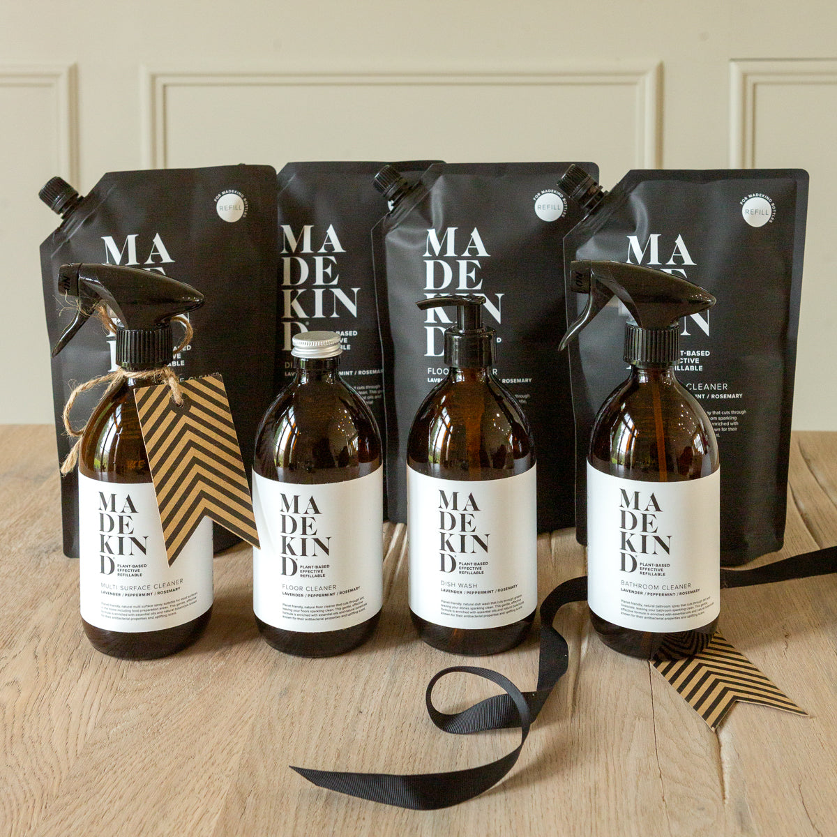 Set of 'MADE KIND' cleaning products including bottles and refill packaging on a wooden surface.