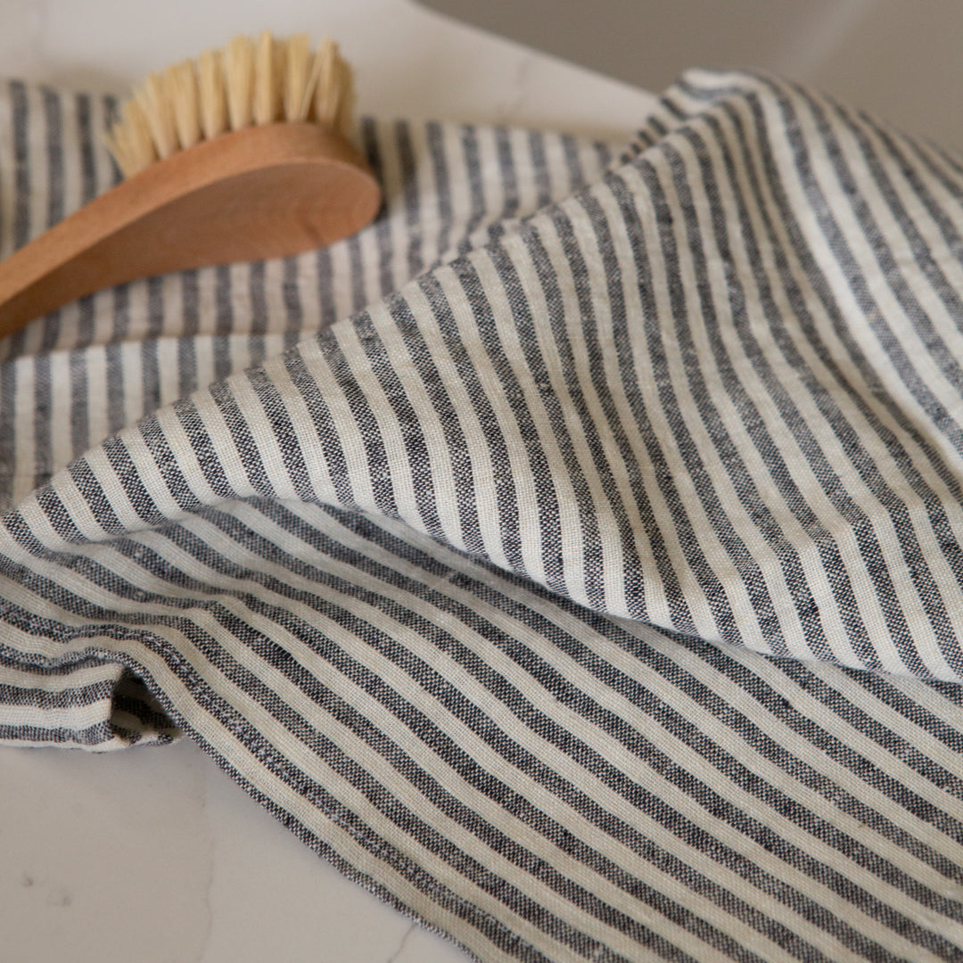 Photo of a woven linen grey striped tea towel with a natural bristle dish brush
