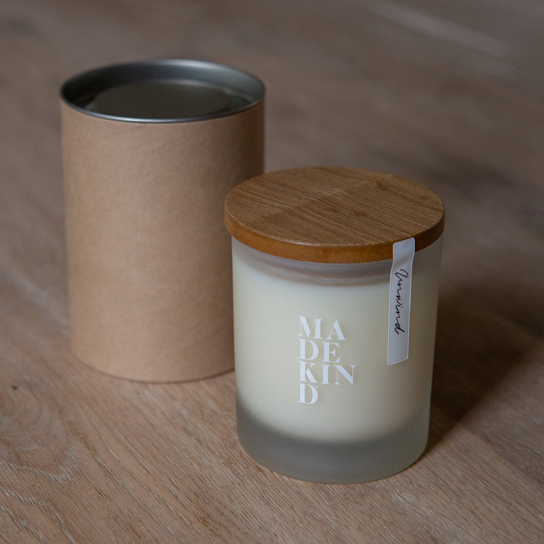 One soy wax candle and gift box tube, on a wooden surface with 'MADEKIND' branding, in unwind blend for relaxation