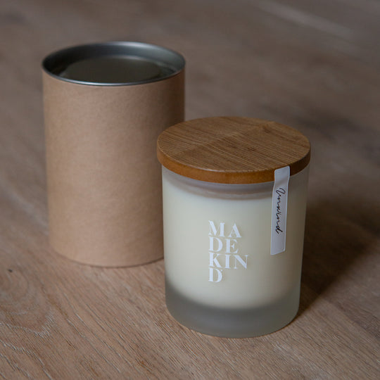 One soy wax candle and gift box tube, on a wooden surface with 'MADEKIND' branding, in unwind blend for relaxation