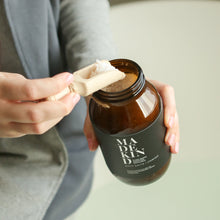 Load image into Gallery viewer, photo of a hand scooping MadeKind bath salts from an amber glass jar containing bath salts

