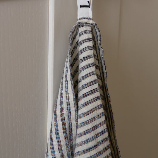 Photo of a woven linen grey striped tea towel hung from a hook