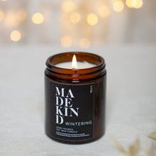 Load image into Gallery viewer, photo of 180ml MadeKind wintering candle, lit and with sparkly lights in the background
