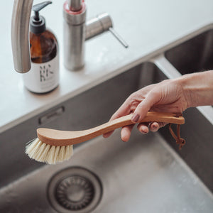 Photo of a Redecker curved handle wooden dish brush being held over a kitchen sink