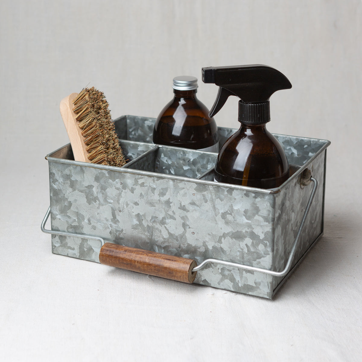 Photo of a brush and two bottles, one with a cap and one with a nozzle, sitting in a cleaning caddy