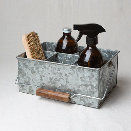 Photo of a brush and two bottles, one with a cap and one with a nozzle, sitting in a cleaning caddy