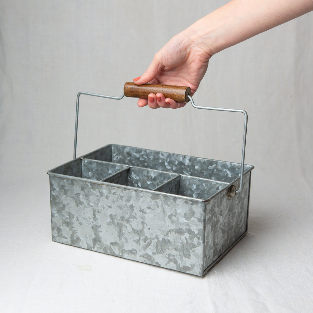 An empty metal caddy with a hand lifting the handle
