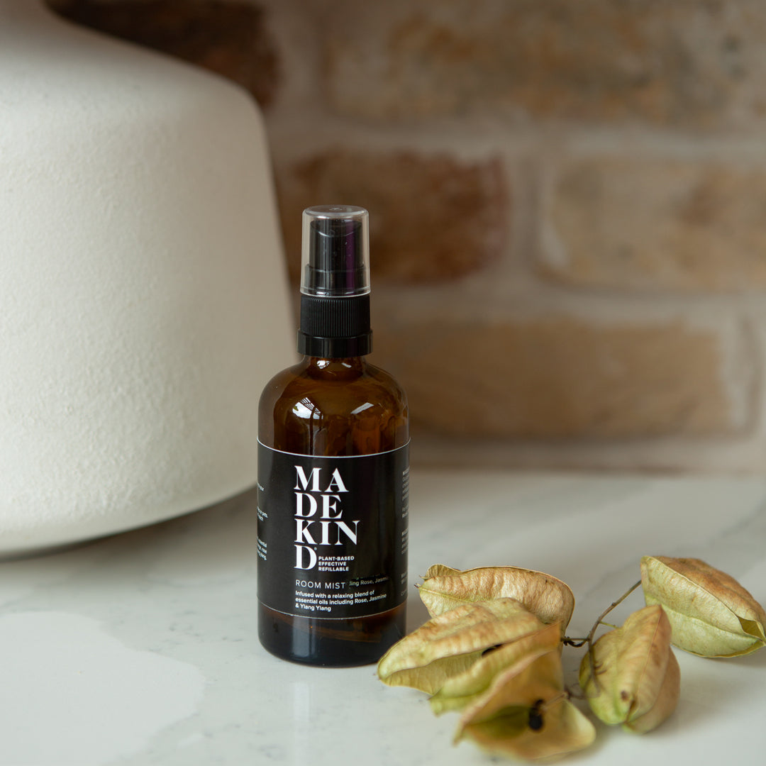 A natural room mist spray bottle labeled 'MADEKIND' with a focus blend of Lavender, Rosemary, and Peppermint, placed on a surface alongside some dried plants.