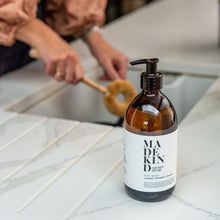 Load image into Gallery viewer, Photo of a MadeKind Natural, eco friendly dish wash in 500ml amber glass bottle next to a kichen sink
